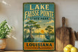 A vintage-style sign for Lake Fausse Pointe State Park in Louisiana, featuring a scenic illustration of a bayou landscape with a bird and palm trees.
