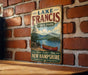 A vintage-style metal sign for Lake Francis State Park in New Hampshire, featuring a scenic image of a lake with a canoe and mountains in the background.