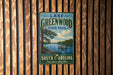 A vintage metal sign for Lake Greenwood State Park in South Carolina, featuring a scenic image of a lake surrounded by pine trees and a boat on the water.