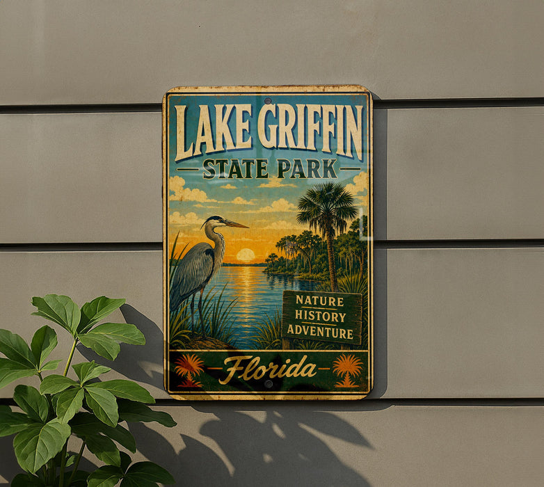 A vintage-style sign for Lake Griffin State Park in Florida, featuring a scenic illustration of a bird, palm trees, and a sunset over the water.