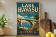 A vintage-style sign for Lake Havasu State Park in Arizona, featuring a scenic illustration of a boat on a lake with a bridge in the background.