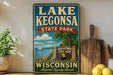 A vintage-style sign for Lake Kegona State Park in Wisconsin, featuring a scenic illustration of a lake, sailboat, and surrounding landscape.