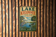A vintage metal sign for Lake Kissimmee State Park in Florida, featuring a scenic illustration of a lake, palm trees, and a bird.