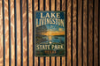 A vintage-style metal sign for Lake Livingston State Park in Texas, featuring a scenic landscape with a sunset over the lake and a bird in flight.