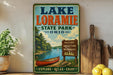 A vintage-style sign for Lake Loramie State Park in Ohio, featuring a scenic image of a lake, canoe, and trees.