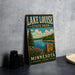 A vintage-style sign for Lake Louise State Park in Minnesota, featuring a scenic illustration of the lake surrounded by pine trees and mountains.