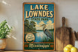 A vintage-style sign for Lake Lowndes State Park in Mississippi, featuring a scenic illustration of a lake, trees, and a bird.