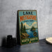 A vintage metal sign for Lake Metigoshe State Park in North Dakota, featuring a scenic landscape with pine trees and a lake.