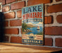 A vintage-style metal sign for Lake Minatare, a state recreation area in Nebraska, featuring a scenic illustration of a lake, mountains, and a sailboat.