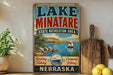 A vintage-style sign for Lake Minatare State Recreation Area in Nebraska, featuring a scenic illustration of a lake, mountains, and a sailboat.