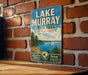 A vintage metal sign for Lake Murray State Park in Oklahoma, featuring a scenic illustration of a lake, trees, and a sailboat.