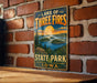 A vintage-style metal sign for Lake of Three Fires State Park in Iowa, featuring a scenic landscape with a lake, mountains, and a sunset.