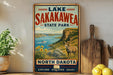 A vintage-style sign for Lake Sakakawea State Park in North Dakota, featuring a scenic landscape with a goat, sunflowers, and a body of water.