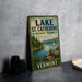 A vintage-style sign for Lake St. Catherine State Park in Vermont, featuring a scenic landscape with a lake, mountains, and a sailboat.