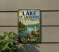 A vintage-style sign for Lake St. Catherine State Park in Vermont, featuring a scenic landscape with a lake, mountains, and a sailboat.