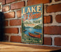 A vintage-style metal sign for Lake St. George, Maine, featuring a scenic illustration of a lake, canoe, and mountains.