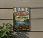 A vintage metal sign for Lake St. George State Park in Maine, featuring a scenic image of a lake with a canoe and mountains in the background.