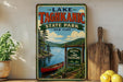 A vintage-style sign for Lake Taghkanic State Park in New York, featuring a scenic image of a lake, pine trees, and a red canoe.