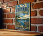 A vintage-style sign for Lake Waramaug State Park in Connecticut, featuring a scenic landscape with a lake, mountains, and a sailboat.