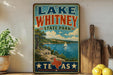 A vintage-style sign for Lake Whitney State Park in Texas, featuring a scenic landscape with a lake, mountains, and a sailboat.