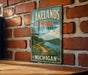 A vintage-style metal sign for Lakelands Trail State Park in Michigan, featuring a scenic landscape with a path leading to a lake surrounded by trees.