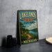 A vintage-style metal sign for Lakelands Trail State Park in Michigan, featuring a scenic landscape with a path leading to a lake surrounded by trees and mountains.