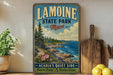 A vintage-style metal sign for Lamoine State Park in Maine, featuring a scenic coastal landscape with pine trees, rocks, and a body of water.