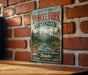 A vintage-style metal sign for the Land of the Yankee Fork State Park in Idaho, featuring a scenic mountain landscape and a river.