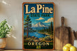 A vintage-style metal sign for La Pine State Park in Oregon, featuring a scenic mountain landscape with pine trees, a lake, and a mountain in the background.