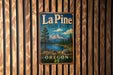 A vintage metal sign for La Pine State Park in Oregon, featuring a scenic mountain landscape with a lake and pine trees.
