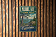A vintage-style metal sign for Laurel Hill State Park in Pennsylvania, featuring a scenic landscape with a river and pine trees.