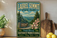 A vintage-style sign for Laurel Summit State Park, featuring a scenic mountain landscape with pine trees and pink flowers.