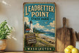 A vintage-style sign for Leadbetter Point State Park in Washington, featuring a lighthouse and a beach scene.