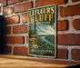 A vintage-style sign for Leffeur's Bluff State Park in Mississippi, featuring a scenic landscape with a river and cliffs.