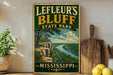 A vintage-style sign for Leffeur's Bluff State Park in Mississippi, featuring a scenic landscape with a river and lush greenery.