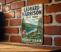 A vintage-style metal sign for Leonard Harrison State Park, featuring a scenic landscape with a river, trees, and mountains.