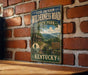 A vintage-style metal sign for the Levi Jackson Wilderness Road in State Park, Kentucky, featuring a scenic illustration of a forest and a cabin.