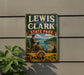 A vintage metal sign for Lewis and Clark State Park in Washington, featuring a scenic landscape with two figures and a compass.