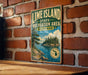 A vintage-style metal sign for Lime Island, Michigan, featuring a scenic landscape with a lake, mountains, and pine trees.