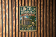 A vintage metal sign for Lincoln Homestead State Park in Kentucky, featuring an illustration of a log cabin and a portrait of Abraham Lincoln.