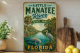 A vintage-style sign for Little Manatee River State Park in Florida, featuring a manatee and a bird in a tropical landscape.