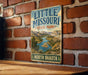 A vintage metal sign for Little Missouri State Park, featuring a scenic landscape with a river and mountains.