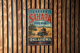 A vintage metal sign for Little Sahara State Park in Oklahoma, featuring an illustration of a person riding an ATV in a desert landscape.