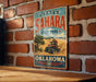 A vintage-style metal sign for Little Sahara State Park in Oklahoma, featuring an illustration of a person riding an ATV in a desert landscape.