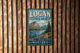A vintage metal sign for Logan State Park in Montana, featuring a mountain landscape and a lake, is displayed on a wooden wall.
