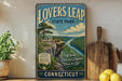 A vintage-style metal sign for "Lovers Leap State Park" in Connecticut, featuring a scenic landscape with a cliff overlooking a river.
