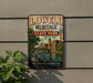 A vintage-style metal sign for Lowell Heritage State Park, featuring a scenic illustration of a river and buildings, mounted on a wall.
