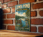 A vintage-style sign for Lums Pond State Park in Delaware, featuring a scenic illustration of the pond and surrounding landscape.