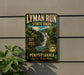 A vintage-style sign for Lyman Run State Park in Pennsylvania, featuring a scenic image of a waterfall surrounded by lush greenery.