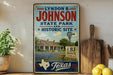 A vintage-style sign for "Lyndon B. Johnson State Park and Historic Site" in Texas, featuring a windmill and a house in the background.